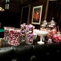 Candy jars and bowls filled with pink and red wrapped sweets on a dark table in a formal room