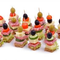 Colorful stacked appetizer skewers with olives, cheese, meat, and bread on a white background
