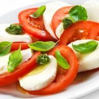 Caprese salad with sliced tomatoes, mozzarella, basil leaves, and pesto on a white plate