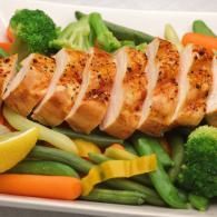Grilled chicken breast slices with steamed broccoli, carrots, green beans, and lemon wedges on a plate