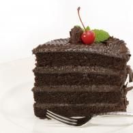 Slice of chocolate cake topped with cherry and mint leaf on a white plate