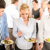 People serving salad at a buffet in a bright office event