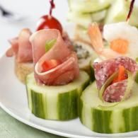 Cucumber slices topped with rolled deli meat and vegetables on a white plate