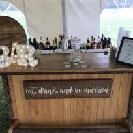 Rustic wedding bar with white script sign reading “eat, drink and be married”