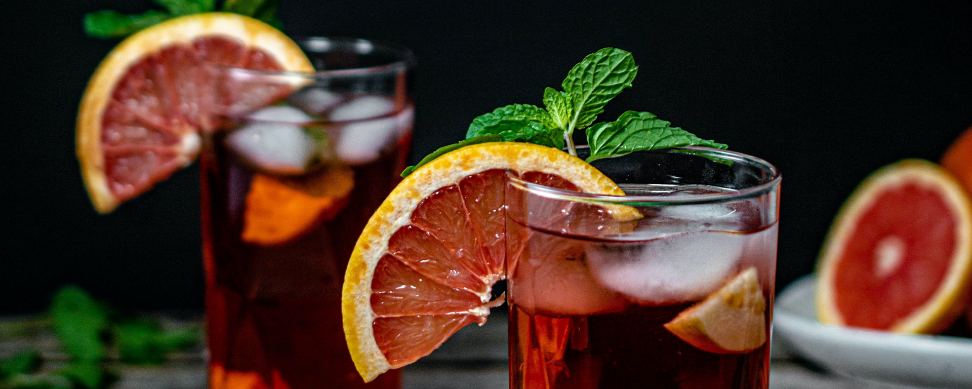 Two glasses of iced red cocktail with orange slices and mint on a dark background