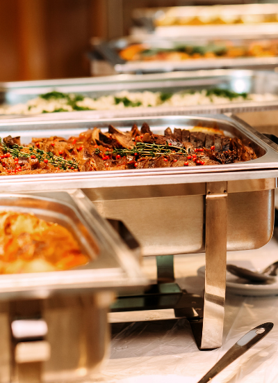 Steam trays of prepared food at a buffet counter, with warm metal pans and serving utensils