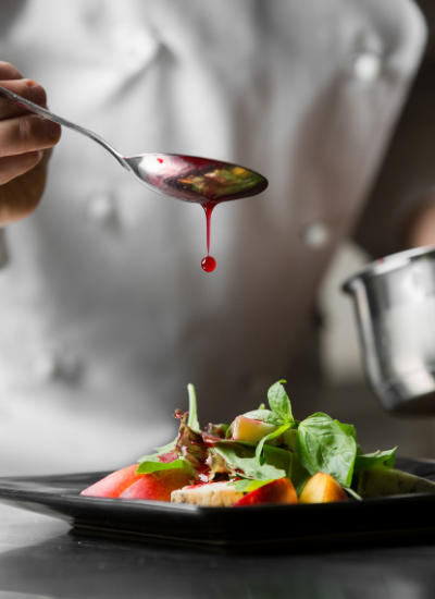 Chef drizzling sauce over a plated gourmet dish on a black plate