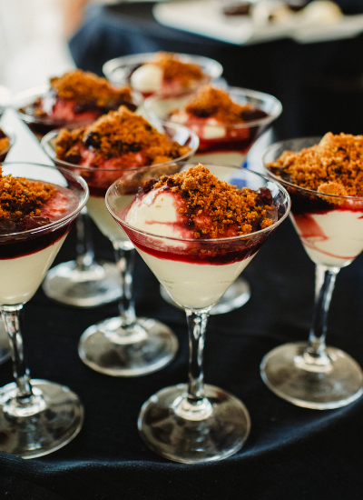 Dessert shooters topped with crumbly garnish arranged on a black tablecloth at a catered event