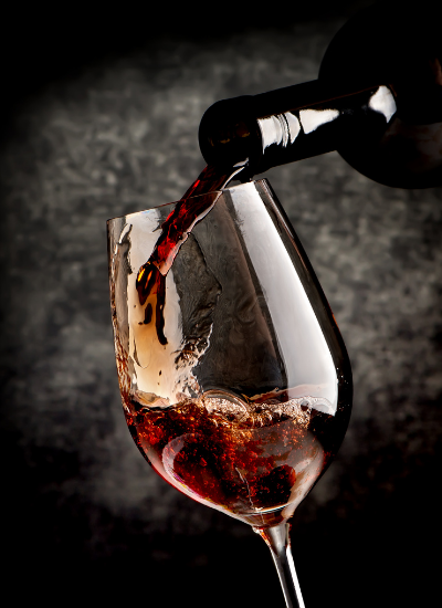 Red wine being poured into a tilted wine glass against a dark background