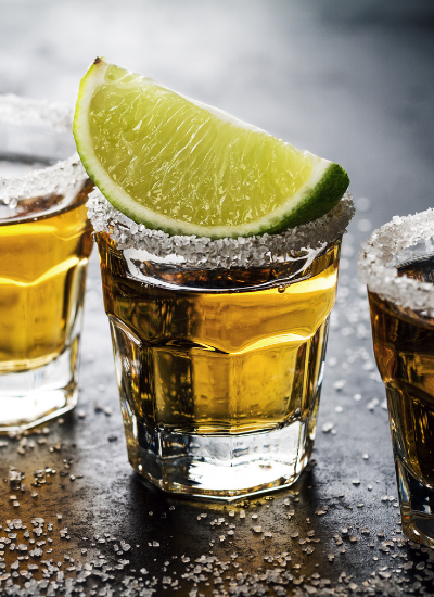 Lime-garnished tequila shot glasses lined on a wet bar counter