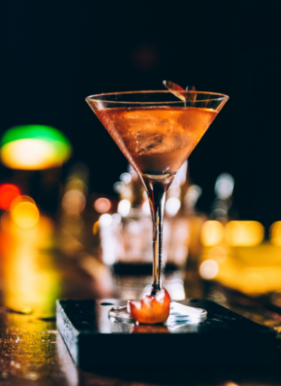 Martini glass on a bar with an orange garnish, warm bokeh lights in the background