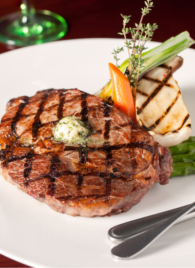 Grilled steak with herb butter and asparagus on a white plate, garnished with rosemary