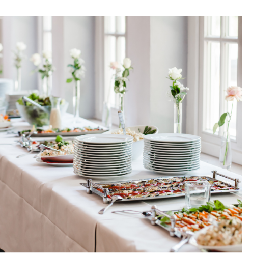 Buffet table with stacked white plates, serving trays, and floral centerpieces in a bright dining room