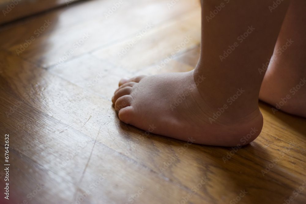 A baby 's bare feet are standing on a wooden floor.