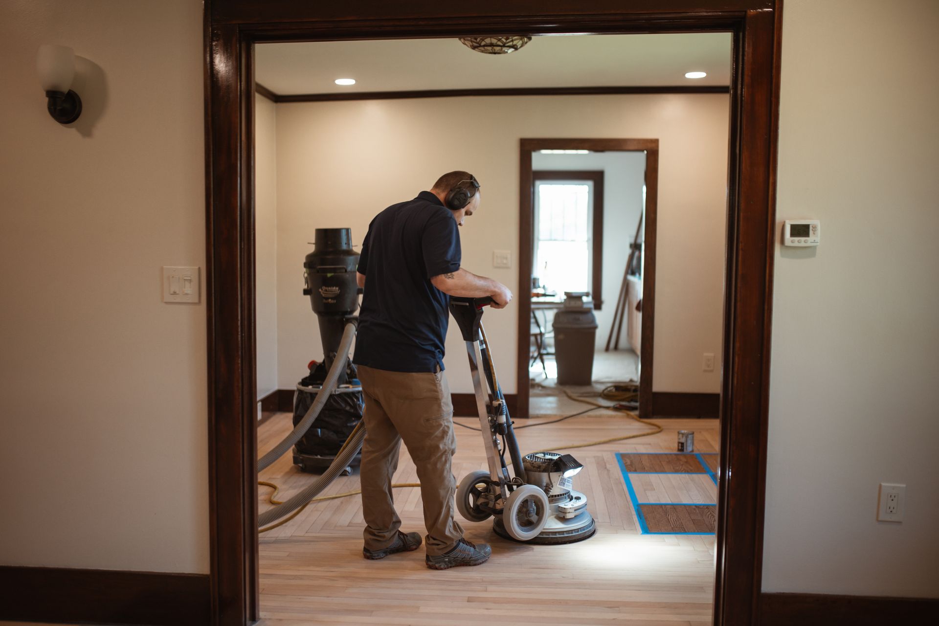 A man is sanding a wooden floor with a vacuum cleaner.