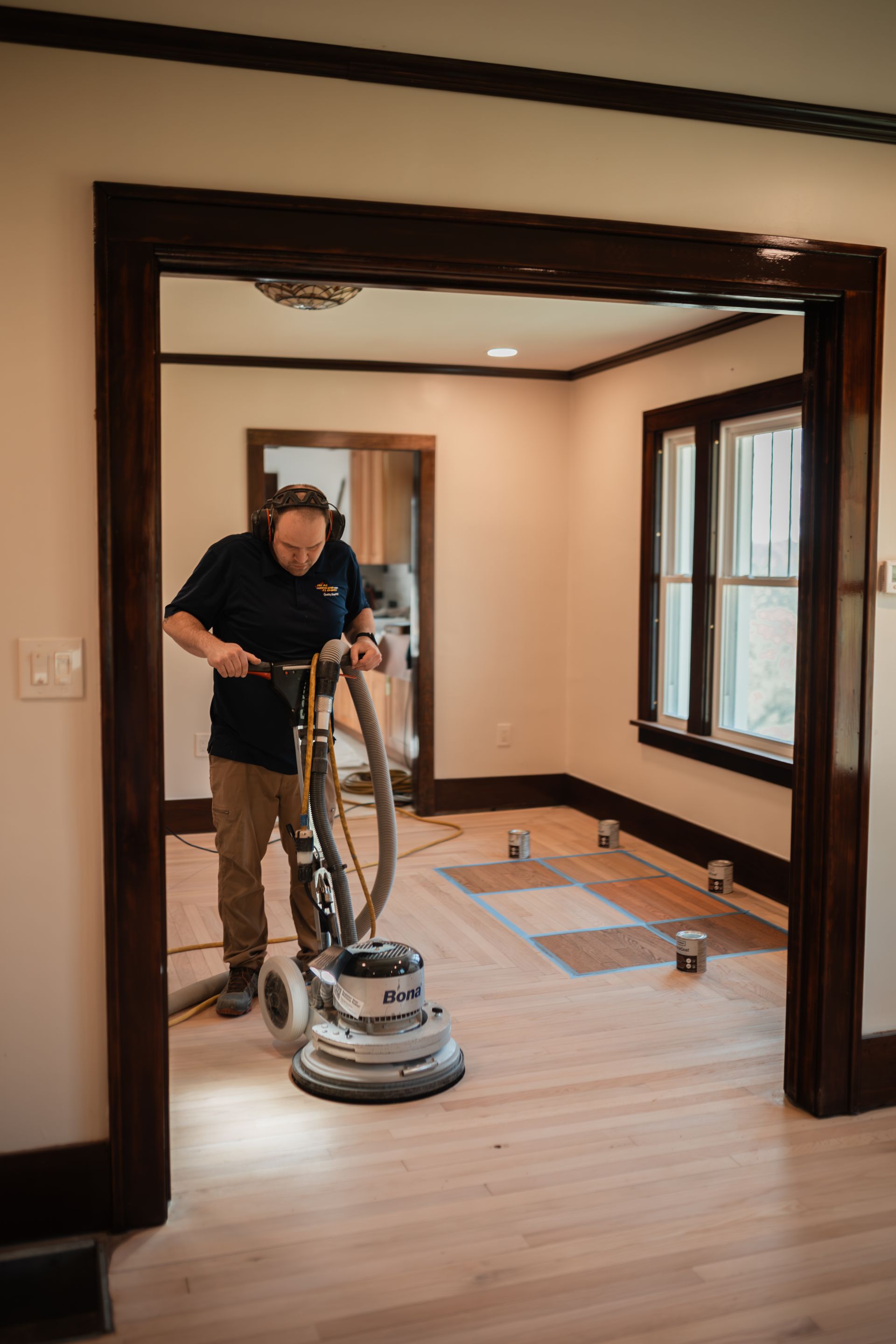 A man is sanding a wooden floor with a machine in a room.