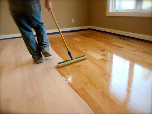 A person is using a broom to finish a wooden floor