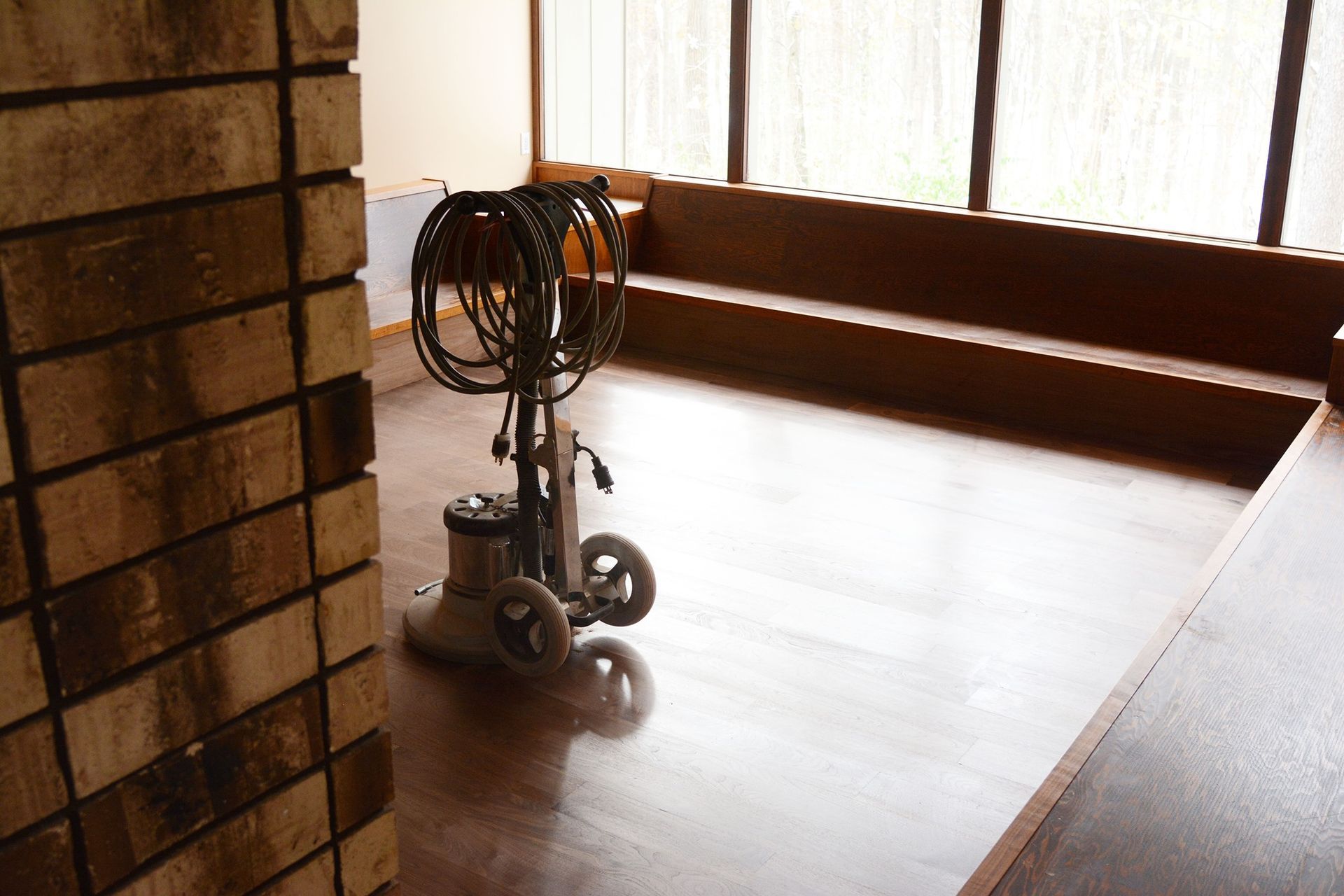 A vacuum cleaner is sitting on a wooden floor next to a brick wall.