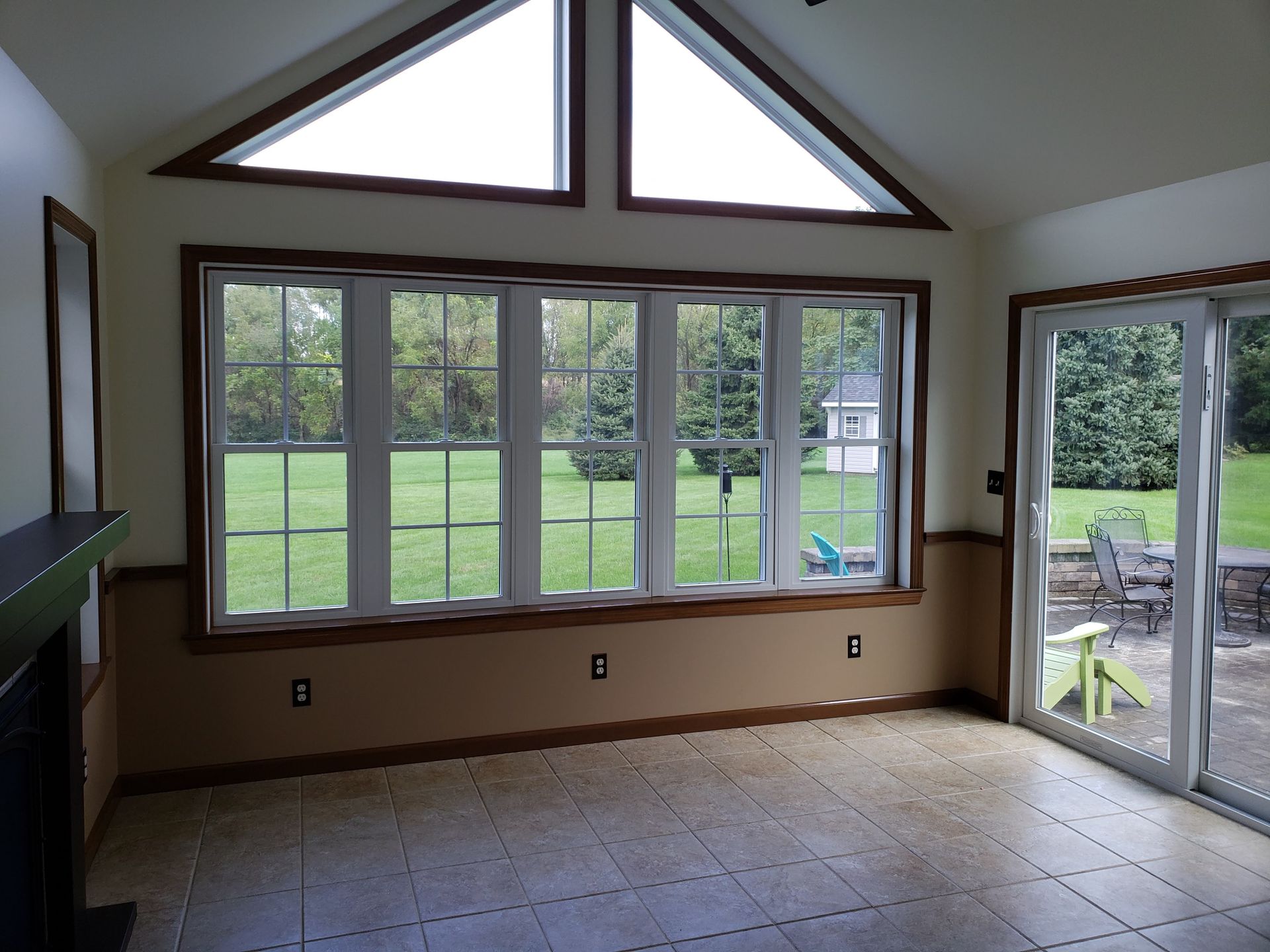 A bright, empty sunroom with tile floors, large grid windows, triangular transom windows, and a sliding glass door.