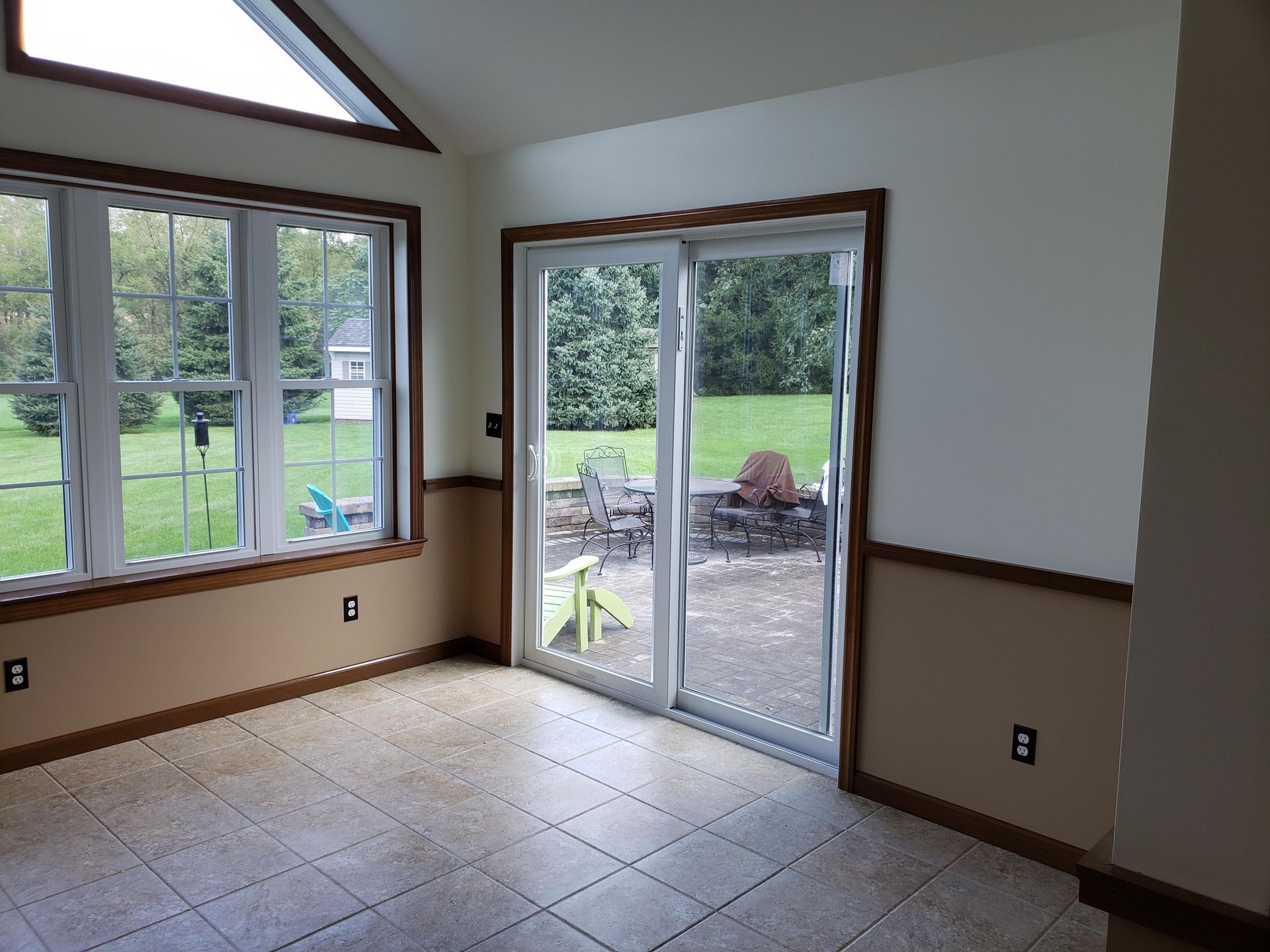 A sunroom with tile floors, beige wainscoting, white walls, large windows, and a glass sliding door opening to a patio.