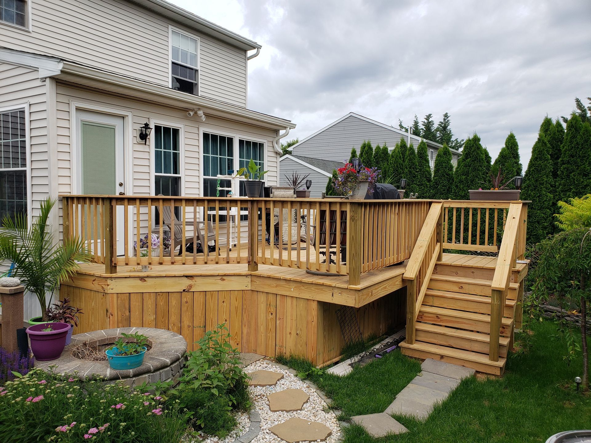A wooden deck with stairs leading up to it is in the backyard of a house.