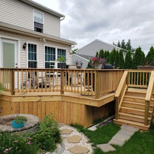 A wooden deck with stairs leading up to it is in the backyard of a house.
