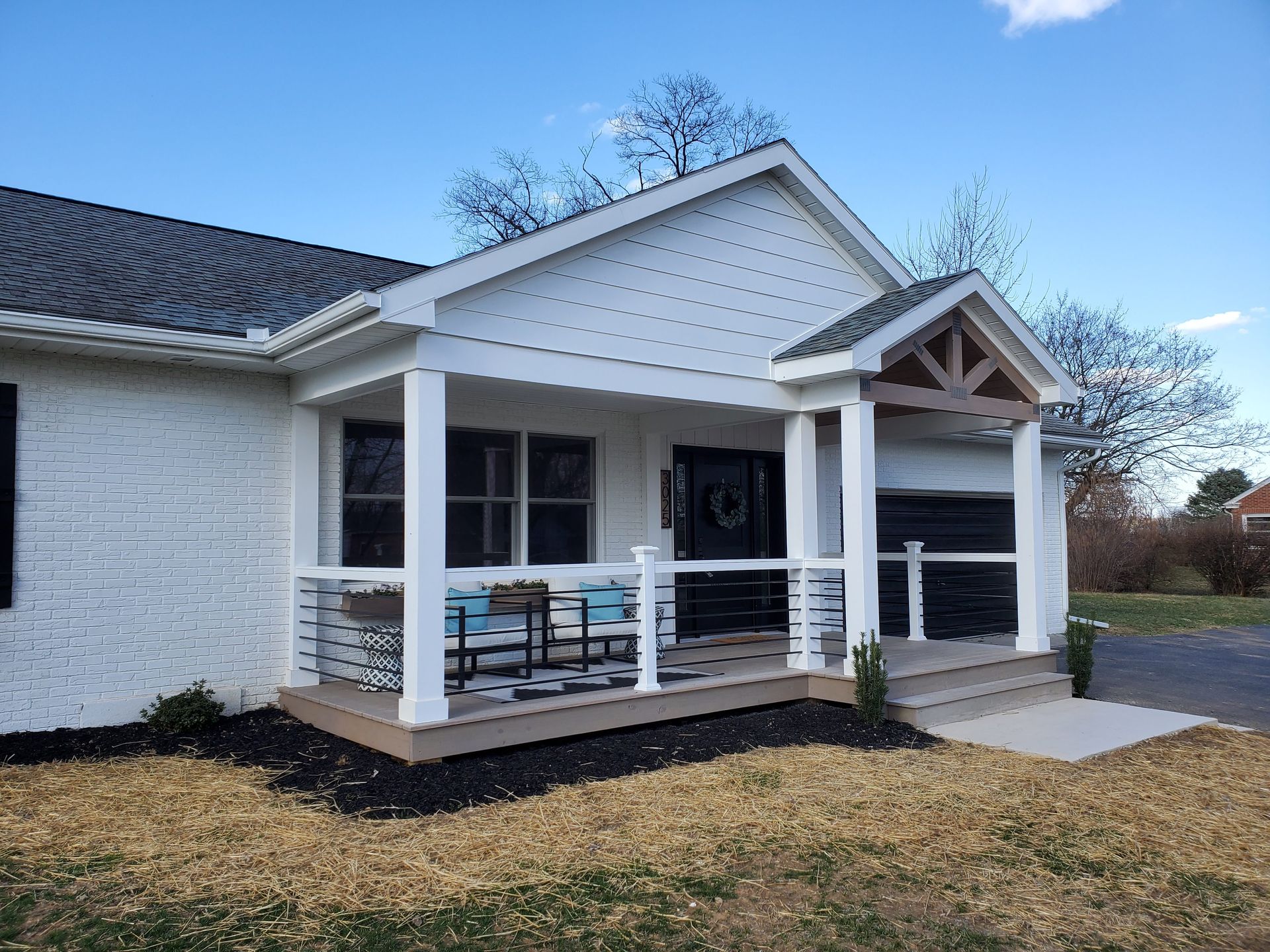 A white brick home with a covered front porch featuring white pillars, modern horizontal railing, and a gabled entrance.