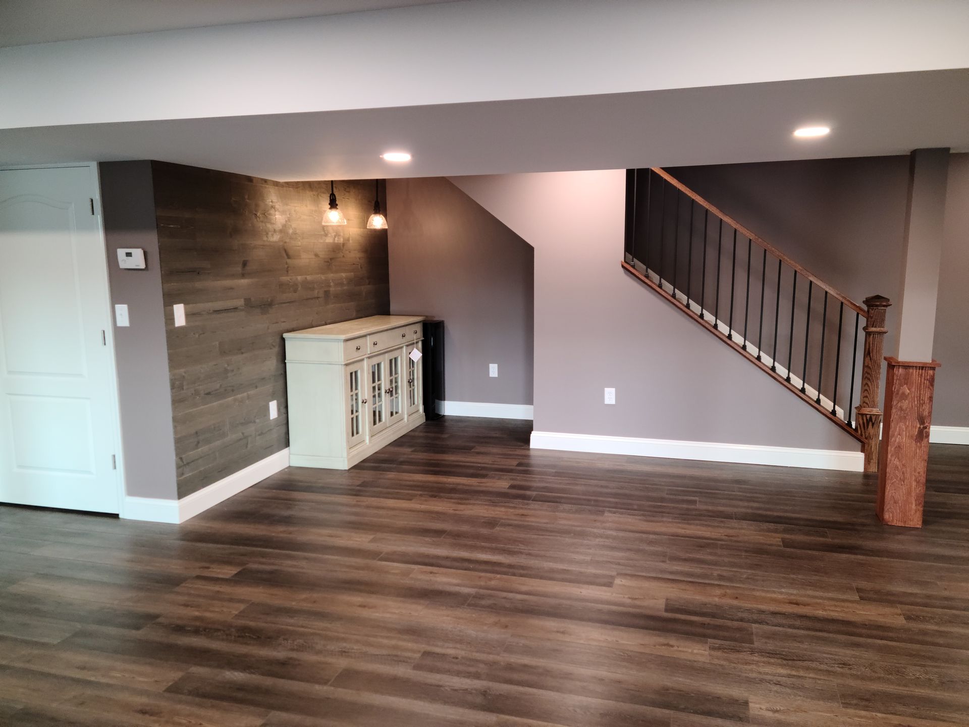 A finished basement area featuring wood-plank flooring, a white cabinet, a wood-paneled feature wall, and a staircase.