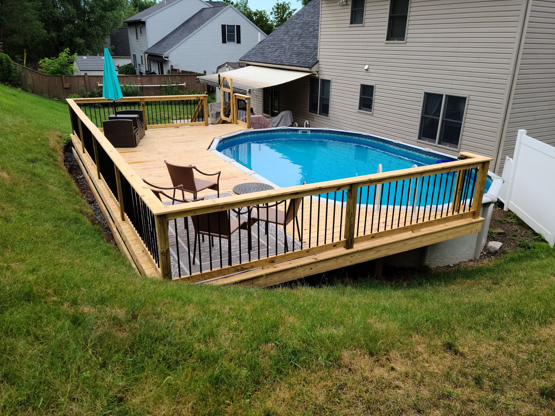 An above-ground pool integrated into a raised wooden deck with railings, situated in a backyard next to a house.