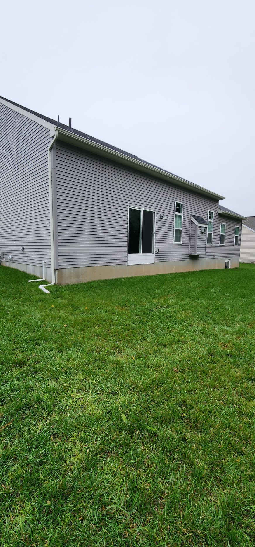 Side view of a house with light grey horizontal siding, a sliding glass door, and windows above a concrete foundation.