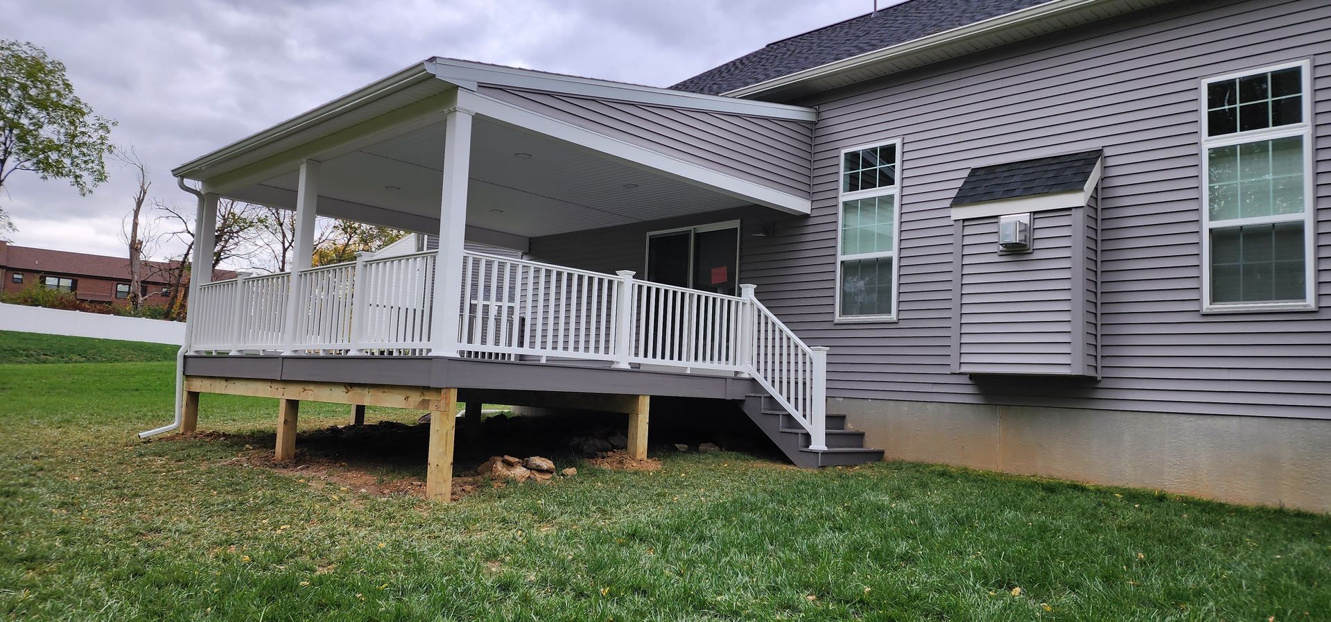 A house exterior featuring a wooden deck with a white railing and covered roof attached to grey vinyl siding.