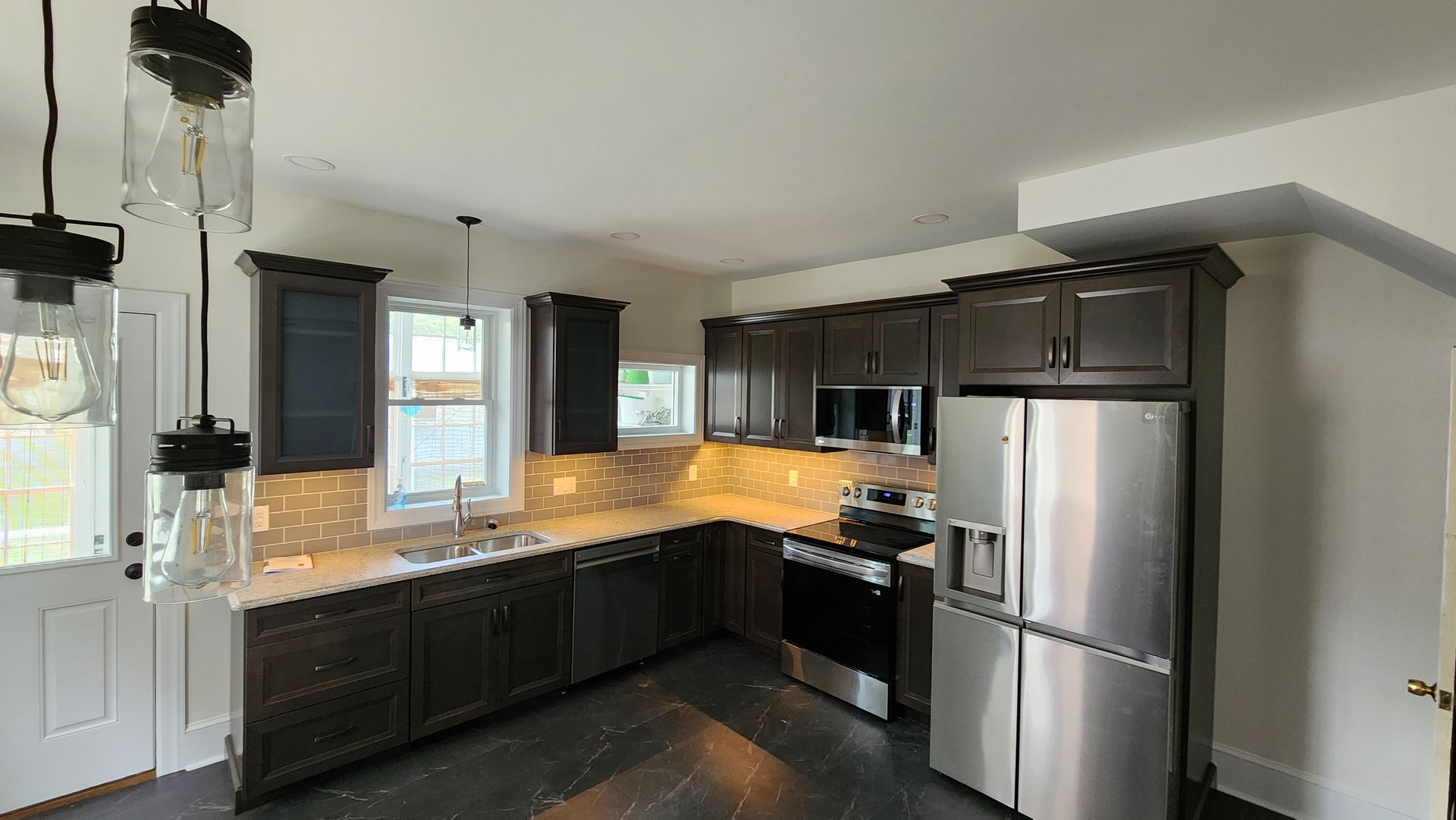 Modern kitchen featuring dark cabinetry, stainless steel appliances, white countertops, and subway tile backsplash.