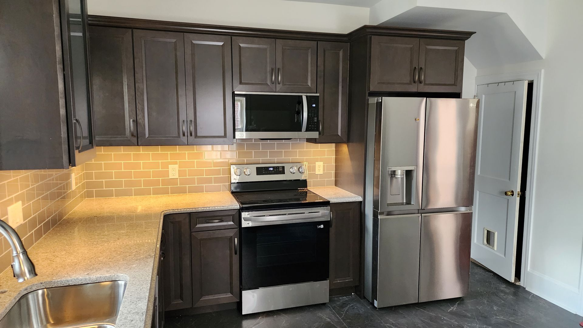 Kitchen with dark brown cabinets, granite countertops, stainless steel appliances, and light gray subway tile backsplash.