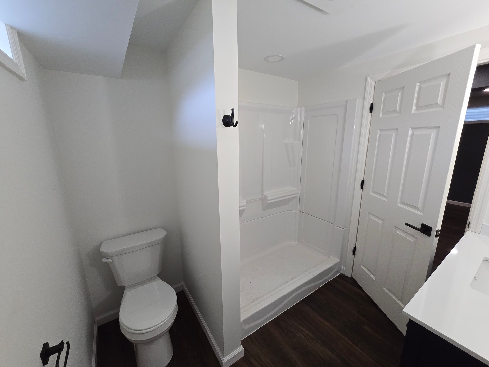 A modern bathroom featuring a white toilet, a walk-in shower with white walls, and a white door with black hardware.