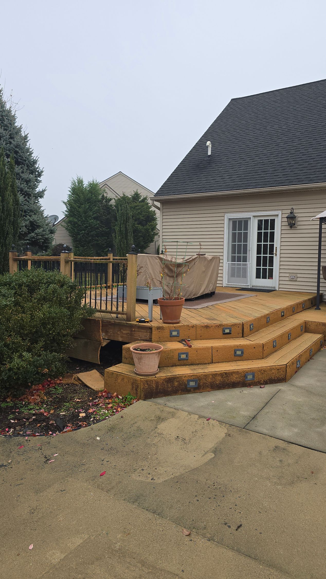 A wooden deck with stair lighting leads to a house with a wavy-patterned exterior wall on a gray, overcast day.