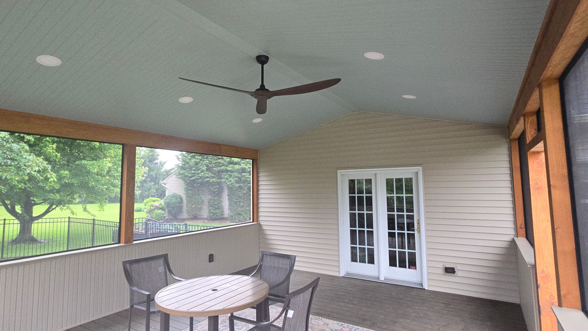 A screened-in porch with a ceiling fan, light fixtures, a small table with chairs, and white French doors.