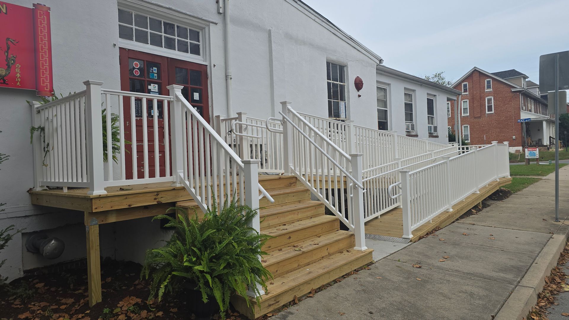 A white building with a new wooden front porch, stairs, and an ADA-compliant ramp with white railings.