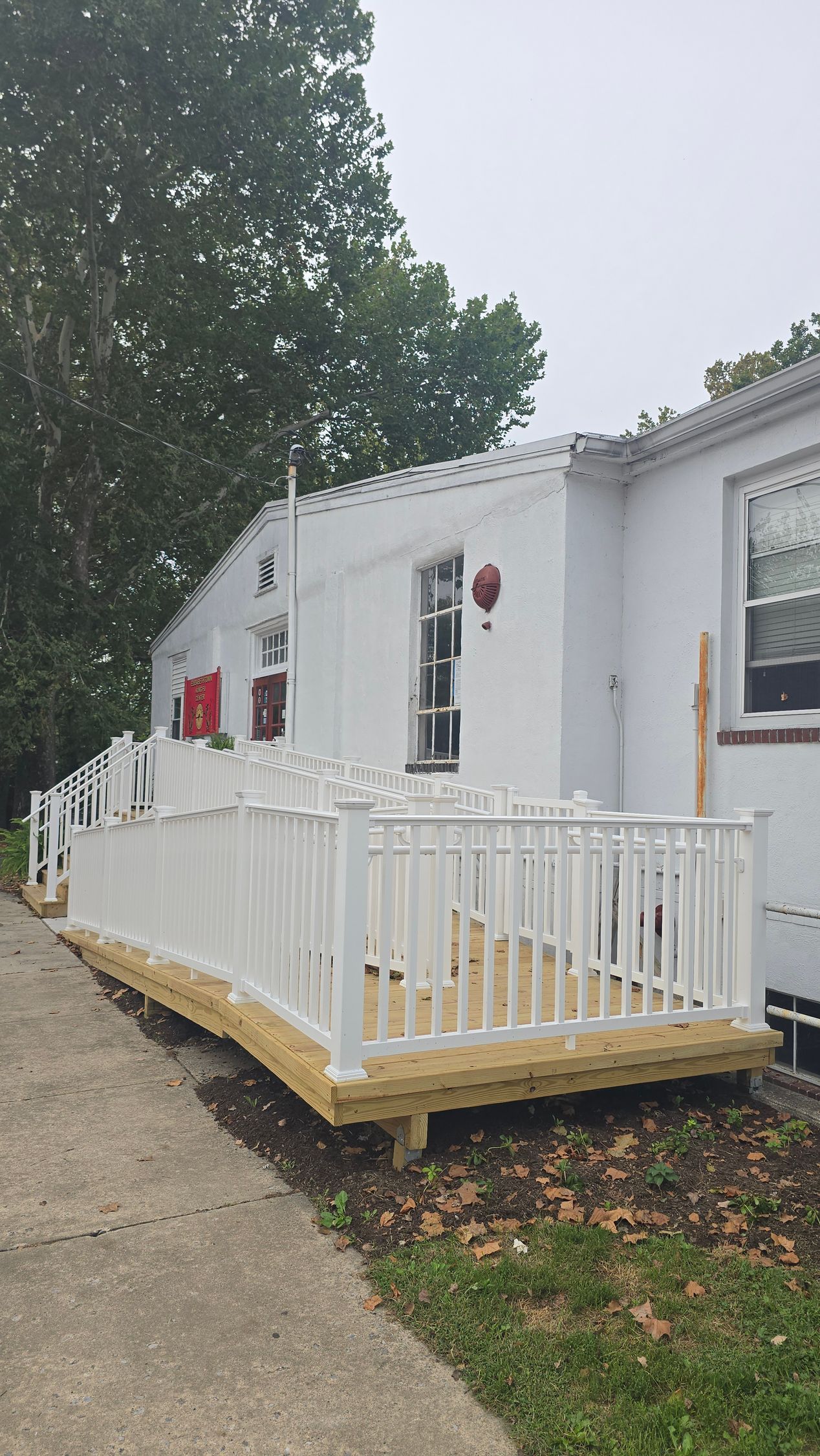 A newly constructed wooden wheelchair ramp with white railings installed against the side of a white building.