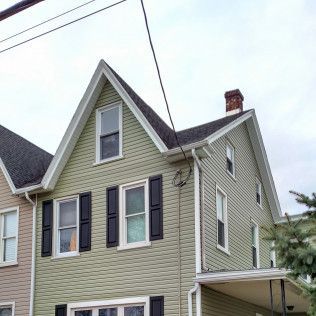A green house with black shutters and a chimney