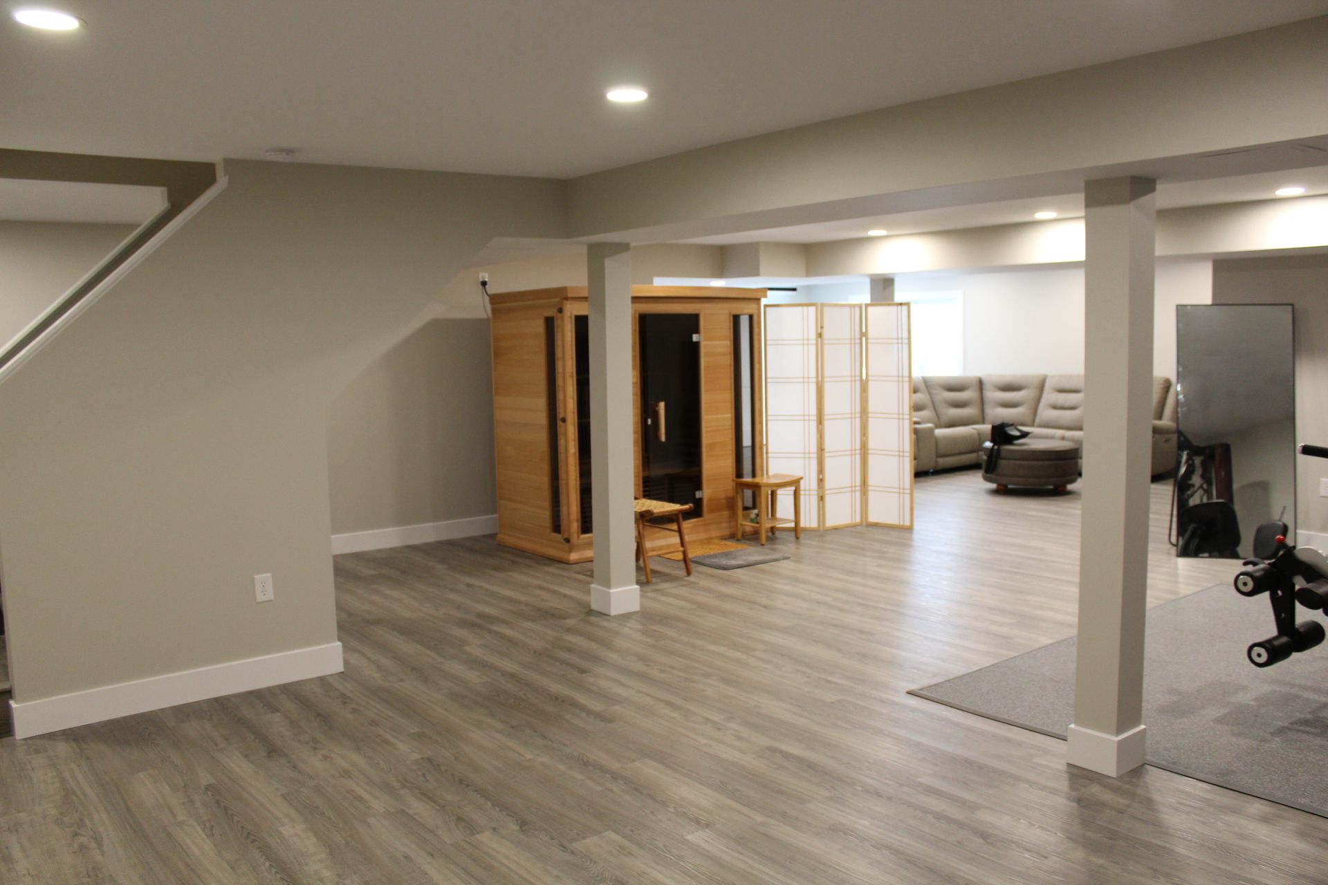 A finished basement featuring light wood floors, a wooden sauna, a room divider, and a seating area with gray furniture.