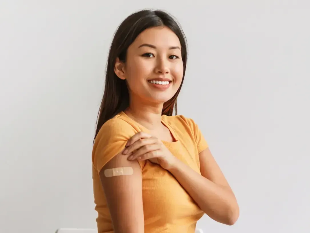 A teen is showing a bandage on her arm where she received a vaccine