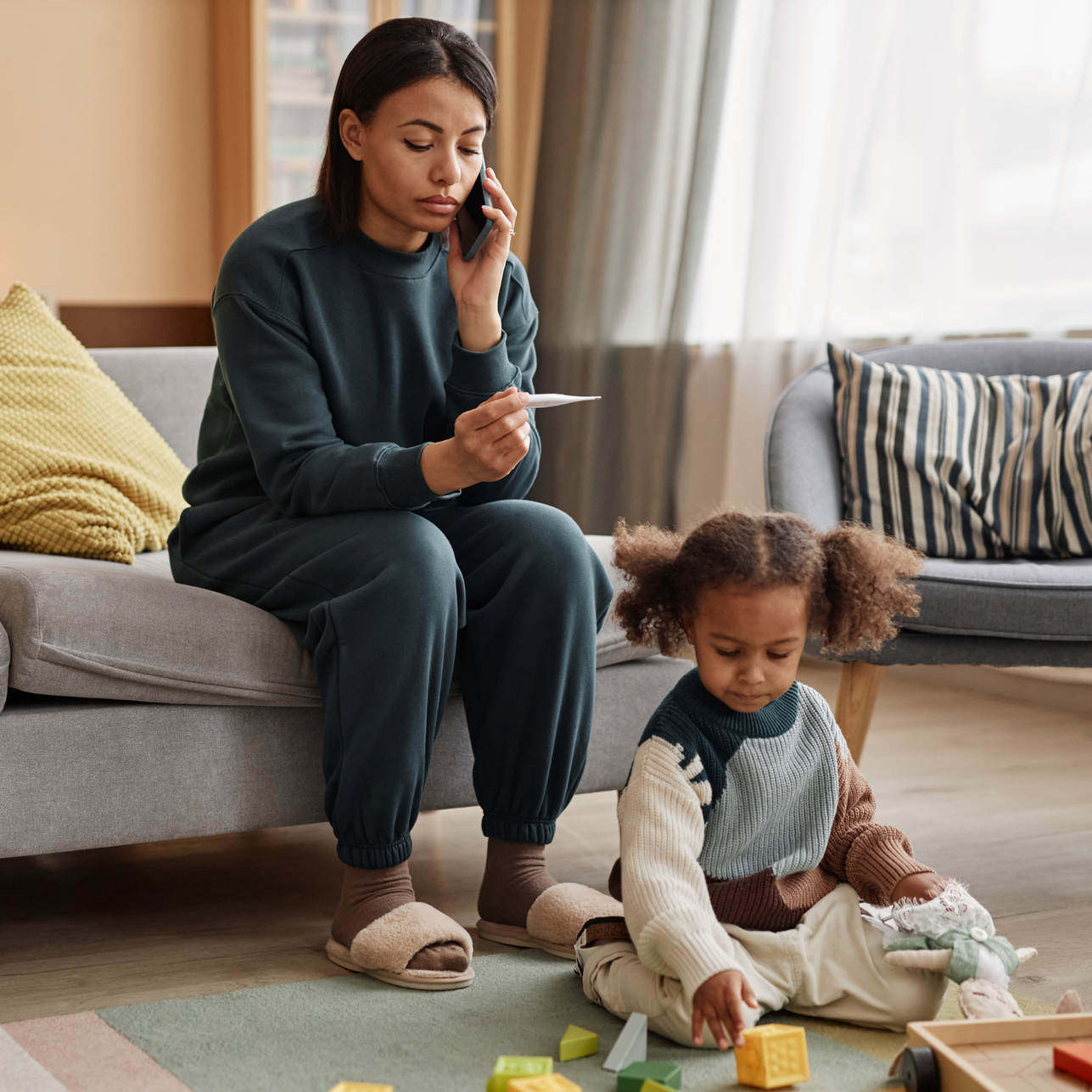 Woman on phone beside toddler playing with blocks in a living room