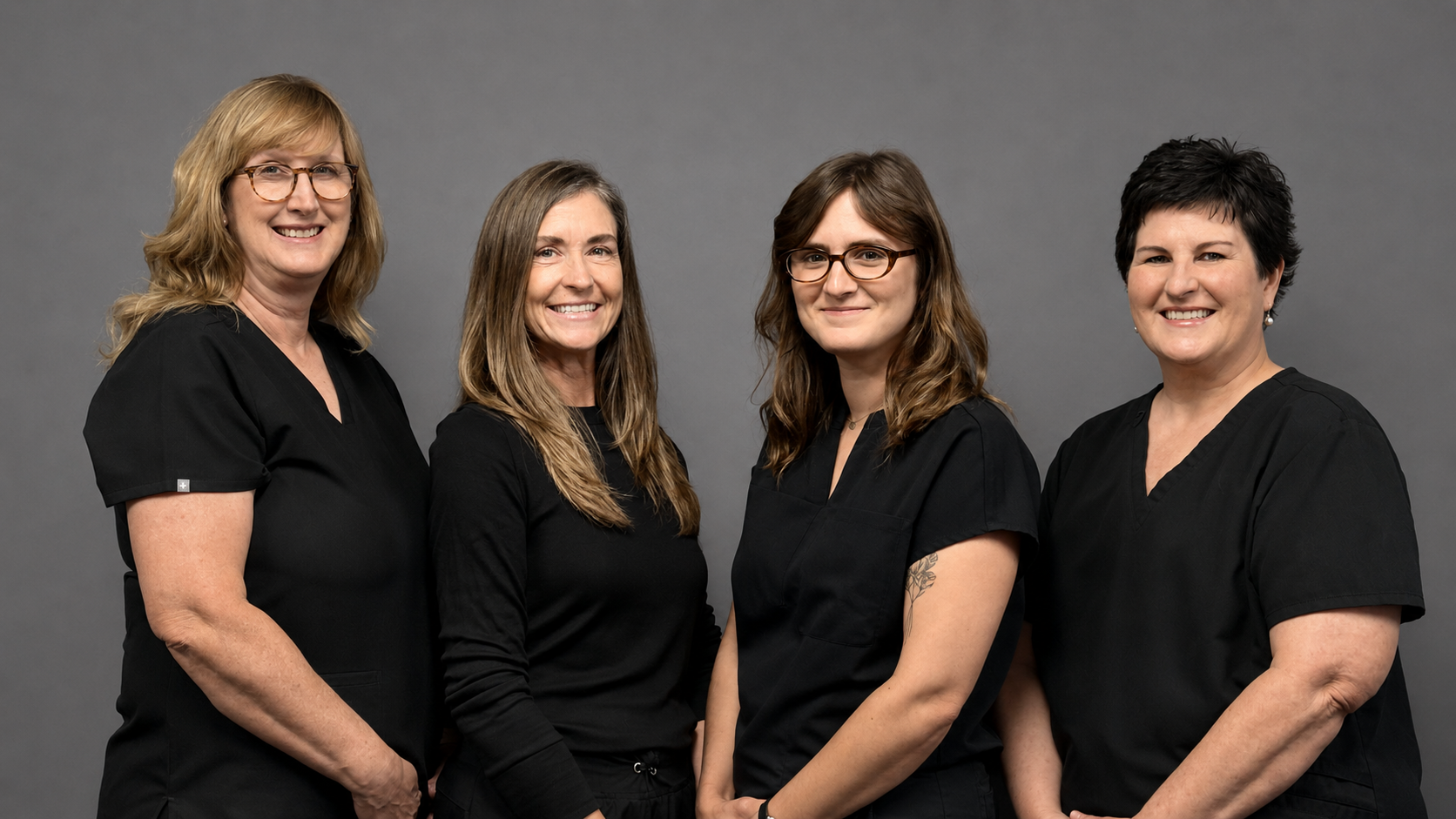 A group of four women wearing black scrubs are posing for a picture.