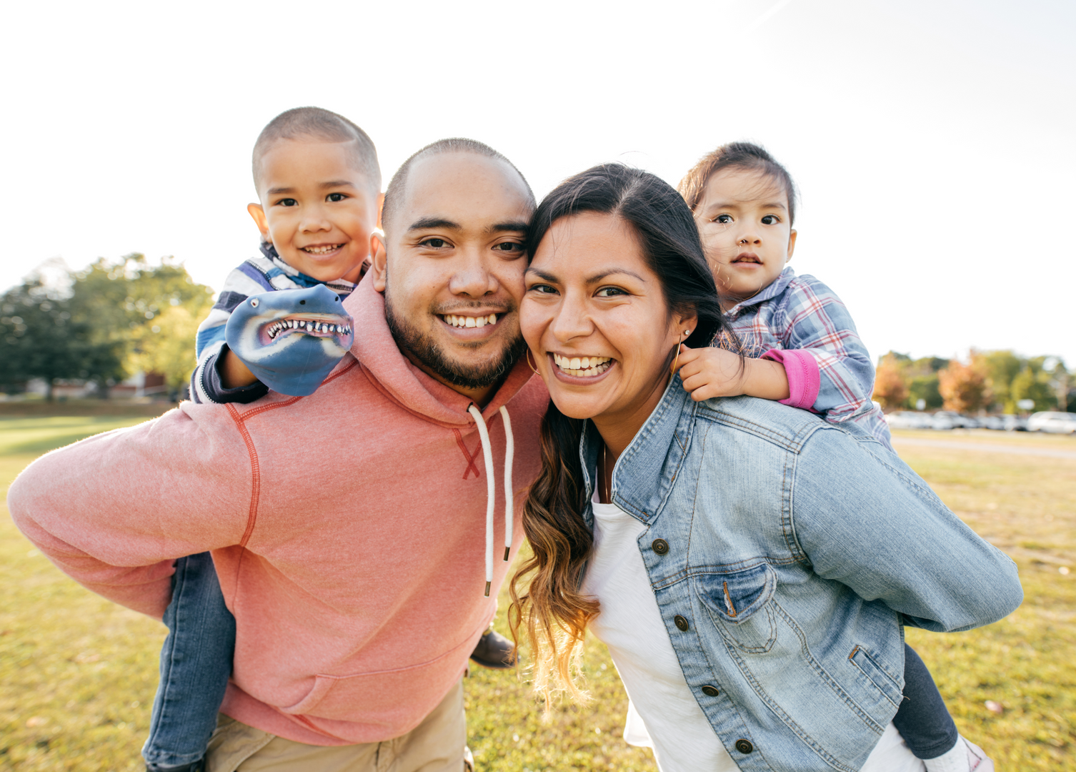 A family is posing for a picture in a park with two children on their shoulders.