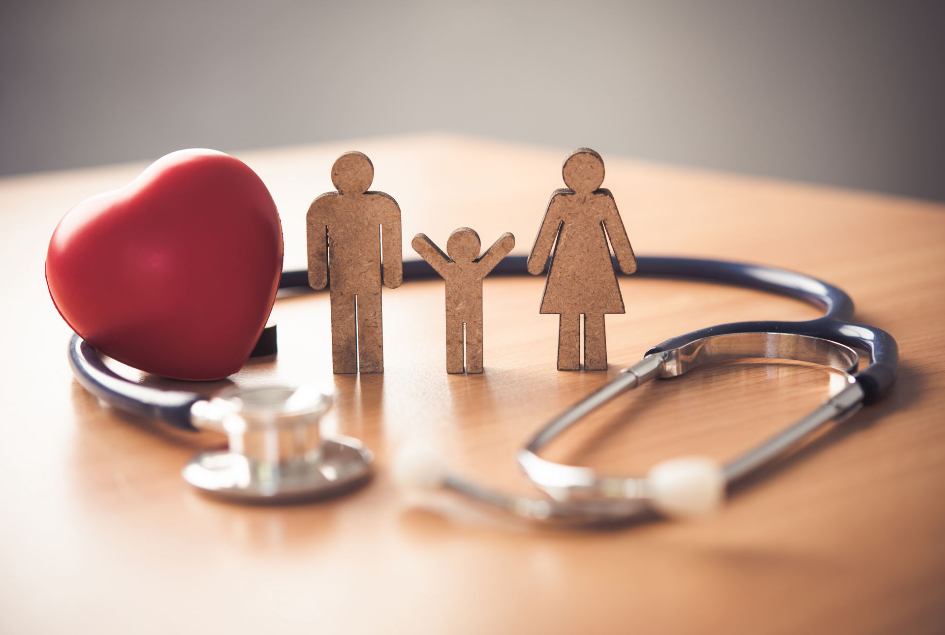 Stethoscope beside a red heart and wooden family figures on a table
