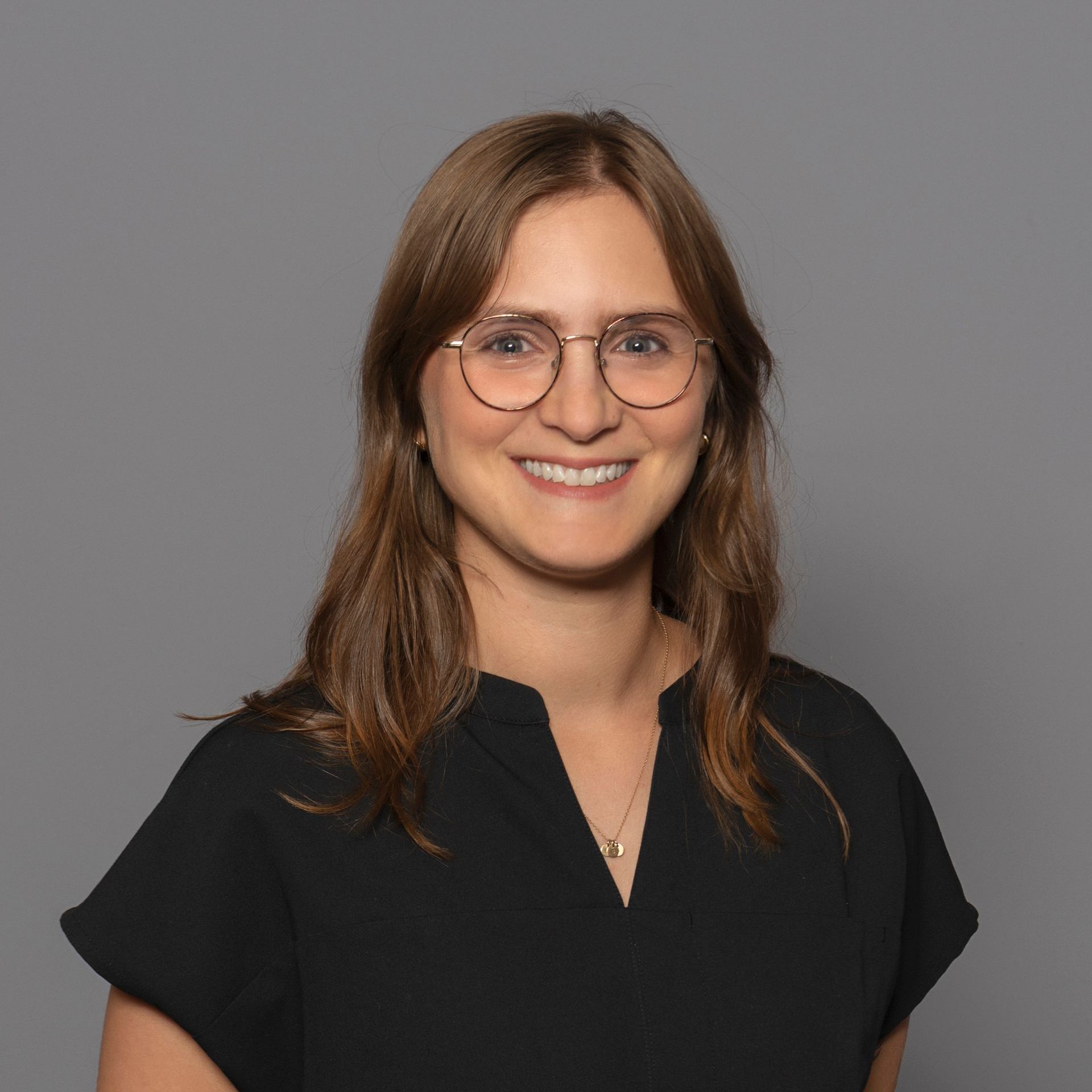 Smiling person with glasses in a black top against a gray background