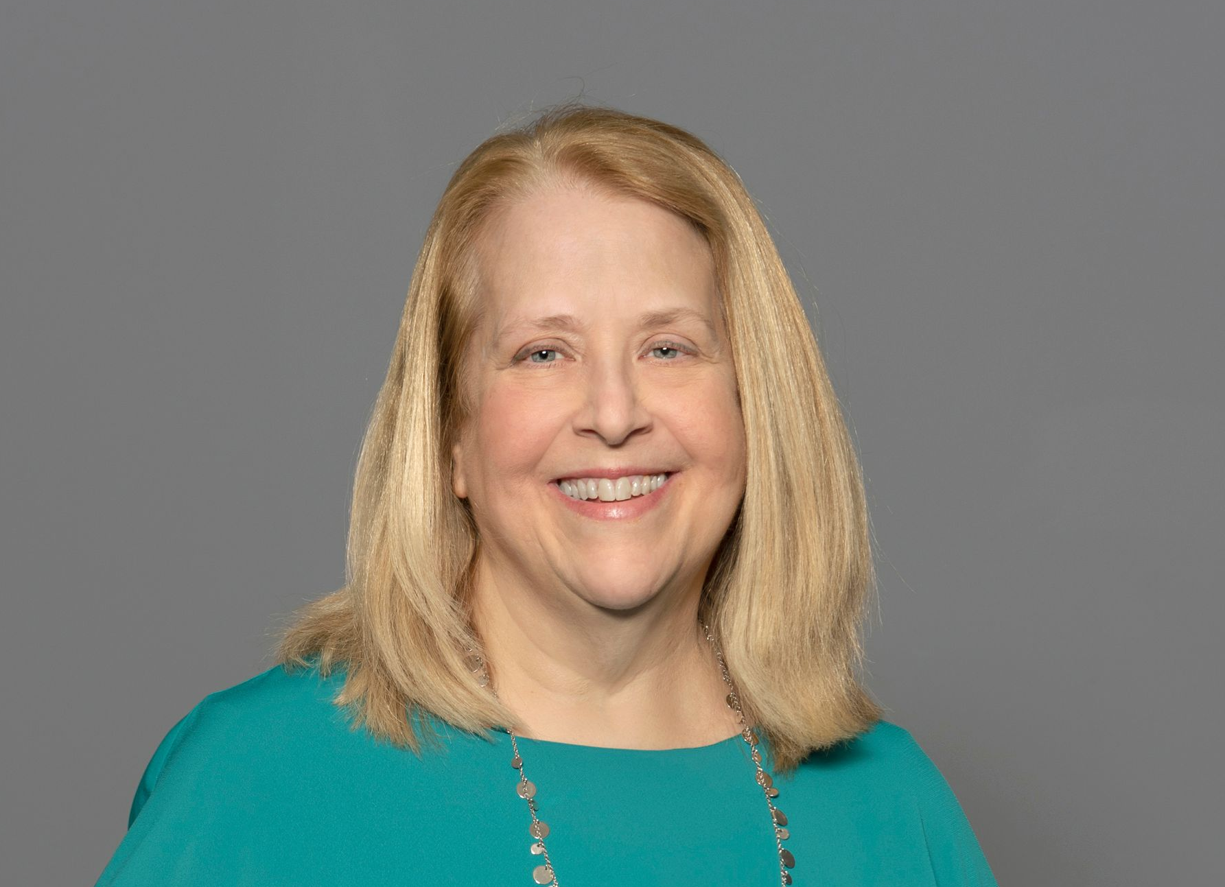 Smiling blonde woman in a teal top against a gray background