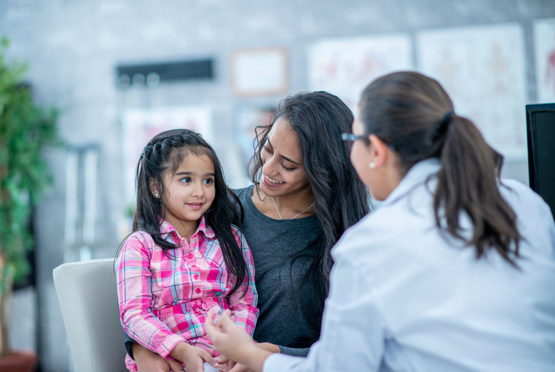 A woman is holding a little girl while talking to a doctor.