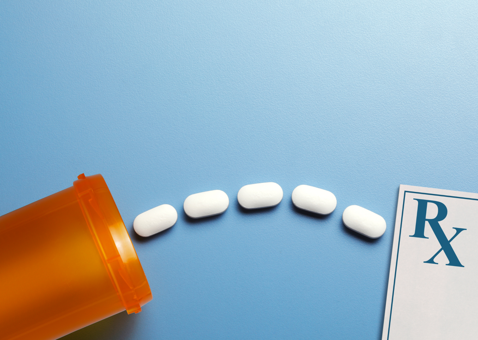 Orange pill bottle spilling white pills beside an Rx prescription card on blue background