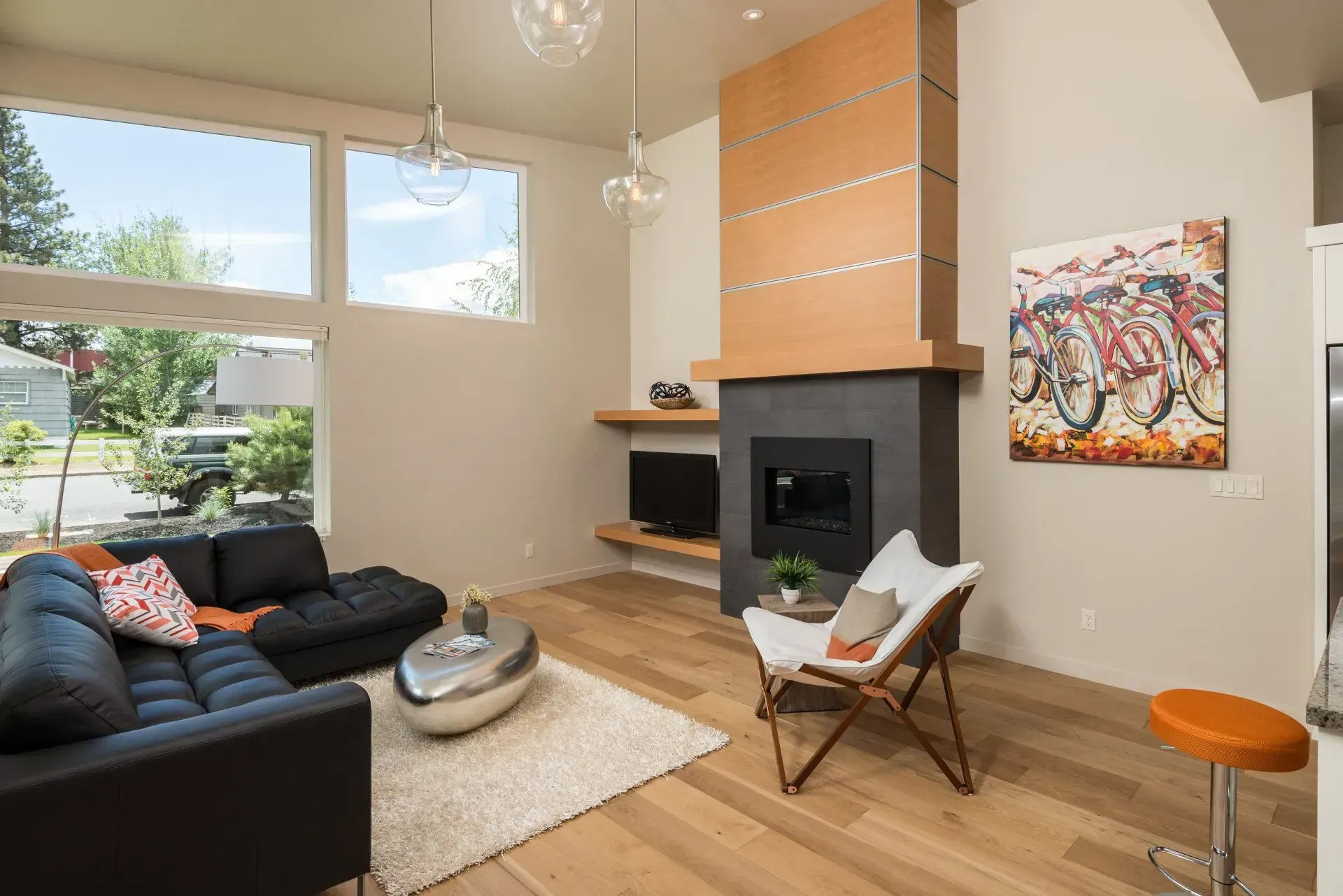 Modern living room with black sofa, fireplace, tan walls, large windows, and colorful wall art.